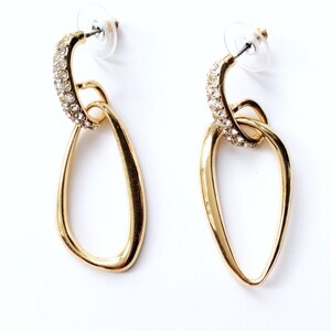 May include: Gold tone earrings with a double oval design. The top oval is encrusted with clear rhinestones.