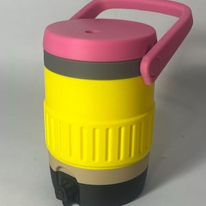 May include: A cylindrical beverage cooler featuring a bright pink lid with a matching pivoting handle, a vibrant yellow body with a textured ribbed midsection, a tan band above the base, and a black bottom section with a small integrated spigot.