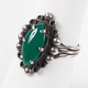 May include: A silver ring with a green gemstone set in a beaded bezel. The ring has a simple band.
