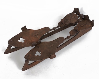 May include: A pair of antique rusty metal ice skates with a cloverleaf design on the blades.
