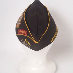 May include: A brown felt military-style hat with a gold trim and a gold embroidered "MISSOURI" on the side. The hat also has a red and gold embroidered patch that says "LIFE MEMBER" and a silver patch that says "V.F.W. 3600".