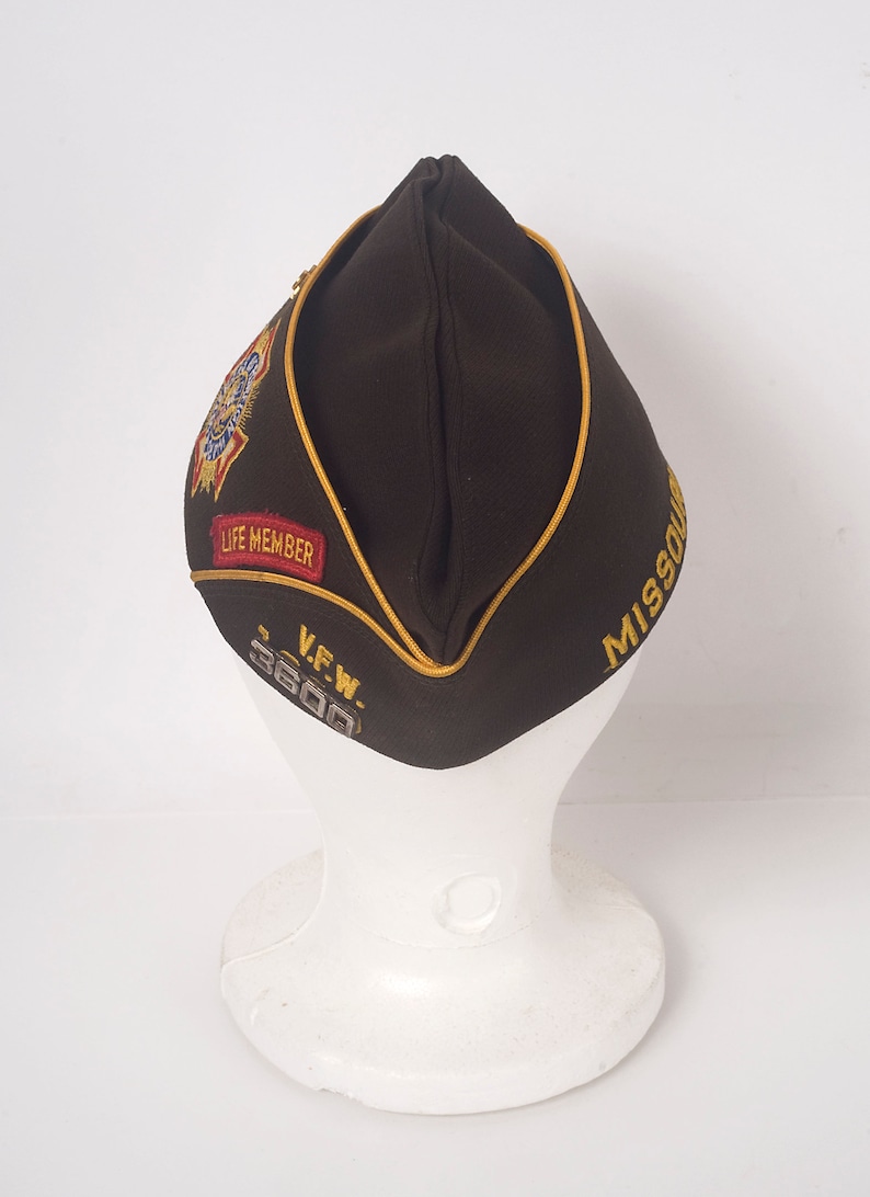 May include: A brown felt military-style hat with a gold trim and a gold embroidered "MISSOURI" on the side. The hat also has a red and gold embroidered patch that says "LIFE MEMBER" and a silver patch that says "V.F.W. 3600".