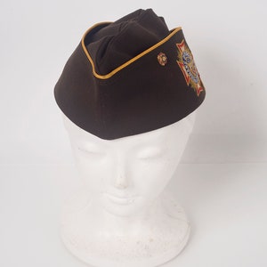 May include: A brown military-style cap with a gold trim and an embroidered patch featuring a red, white, and blue star with the words "American Legion" around it.