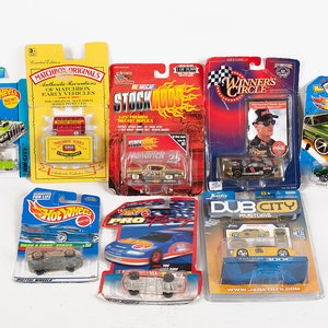 Puede incluir: Una colección de coches de juguete en sus embalajes. Los coches son de diferentes marcas, incluyendo Hot Wheels, Matchbox y Stock Car. Los coches son de varios colores, incluyendo rojo, verde, azul y amarillo. El embalaje es colorido y presenta imágenes de los coches.