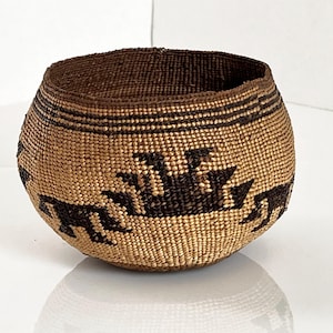 Può includere: Cesto tessuto a mano di forma arrotondata, con una combinazione di colori beige naturale e marrone scuro. Il cesto presenta un motivo decorativo di forme geometriche marroni scure e strisce orizzontali. Il bordo e l'interno sono marrone scuro.