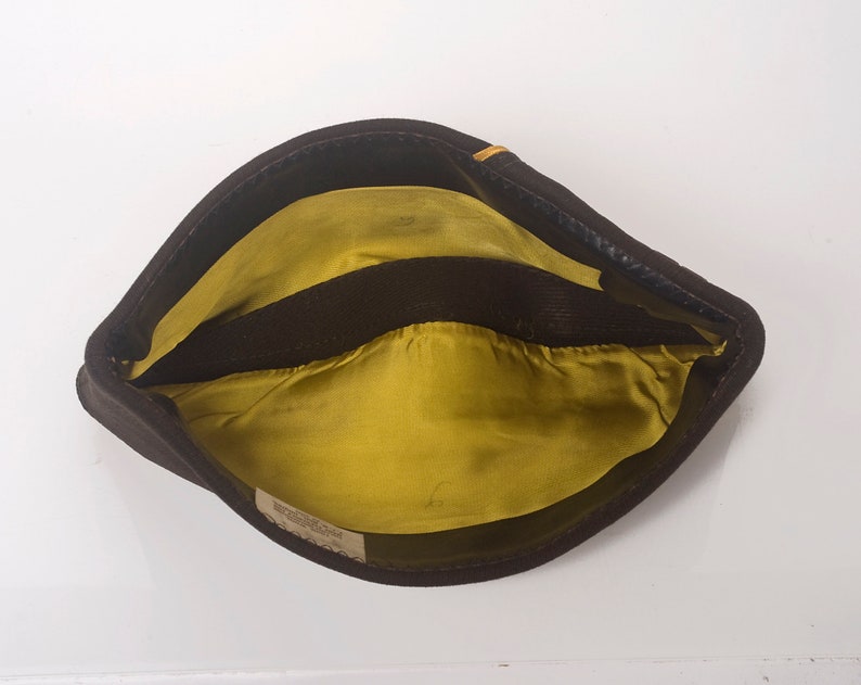 May include: A brown felt hat with a yellow lining and a black band. The hat has a small label on the inside.