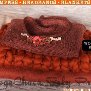 May include: A set of three knitted baby props in shades of rust and brown. The set includes a chunky knit blanket, a smaller knit blanket, and a knitted headband with a flower embellishment. The headband is decorated with a red flower and green leaves.