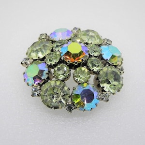 May include: A vintage brooch with a cluster of iridescent green, blue, and clear rhinestones set in silver tone metal.