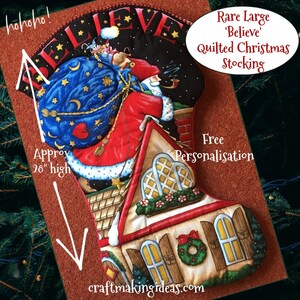 May include: A large quilted Christmas stocking featuring a Santa Claus figure climbing a chimney with a bag of gifts. The stocking is decorated with a red and white house, a wreath, and the word "Believe". It is approximately 71 cm high and includes free personalisation.