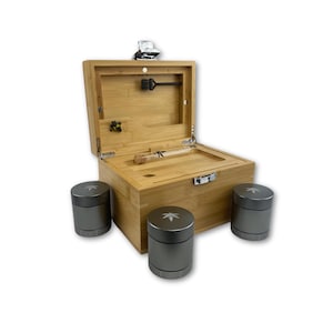 May include: A bamboo box with an open lid, showing a glass tube and a small brush. Three grey cylindrical containers with a leaf design are in front of the box. The box has a silver latch and hinges.