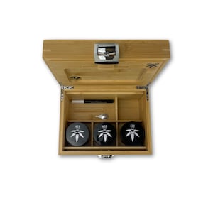 Könnte beinhalten: Offene Bambusbox mit einem Schloss und drei schwarzen Behältern mit einem weißen Blattdesign und dem Wort "ZZZ" darauf. Die Box enthält außerdem ein kleines silbernes Werkzeug und einen schwarzen Stift.