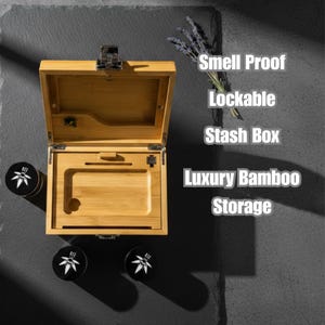 Puede incluir: Caja de almacenamiento de bambú abierta con cerradura, con una bandeja y un compartimento. El texto en la imagen dice "Smell Proof, Lockable, Stash Box, Luxury Bamboo Storage." También se ven dos recipientes negros con un diseño de hoja blanca.