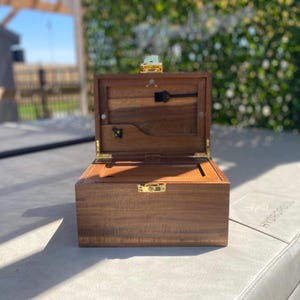 May include: A wooden box with a hinged lid and a brass latch. The box is open and the inside is empty.