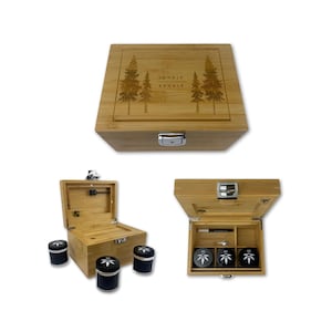 Könnte beinhalten: Eine Bambusbox mit silbernem Verschluss, graviert mit zwei Kiefern und den Worten "INHALE EXHALE". Die Box öffnet sich und zeigt ein Fach mit drei schwarzen Grinders und einem kleinen Werkzeug. Drei weitere schwarze Grinders sind ebenfalls sichtbar.