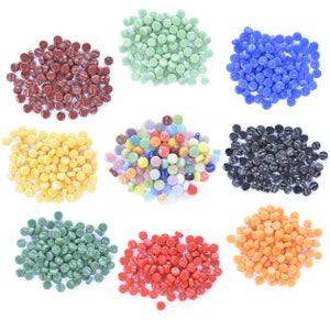 May include: Assortment of small, round glass tiles in various colours, including red, green, blue, yellow, black, and multi-coloured. The tiles are arranged in rows on a white background.