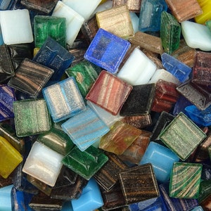 May include: A close-up of a variety of small, square glass tiles. The tiles are in a range of colours, including blue, green, brown, red, and gold. The tiles are arranged in a random pattern.