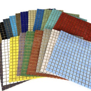 May include: A collection of square mosaic tile sheets arranged in a fan pattern. The tiles feature a grid of small, individual squares in a variety of colours including red, blue, yellow, green, white, black, brown, and tan with a textured finish.