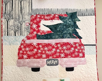 May include: A red truck with a Christmas tree in the back, a red mug with a Christmas tree design, a clear glass jar with a Christmas tree design, and a wooden sign with a red truck and Christmas tree design that says "Be Merry!"