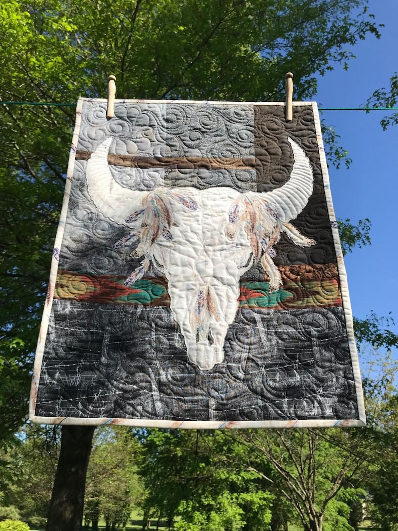 Buffalo skull quilted wall hanging shown on clothesline from low angle.