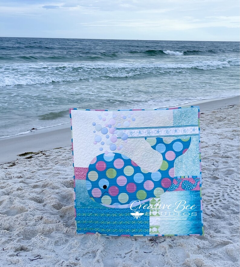 Bubbles the Baby Whale quilt shown at the beach with surf in the background.