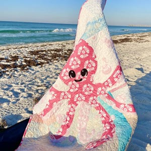 Beach photo of baby octopus applique quilt made with both sides of pink fishbone and sand dollar fabric.