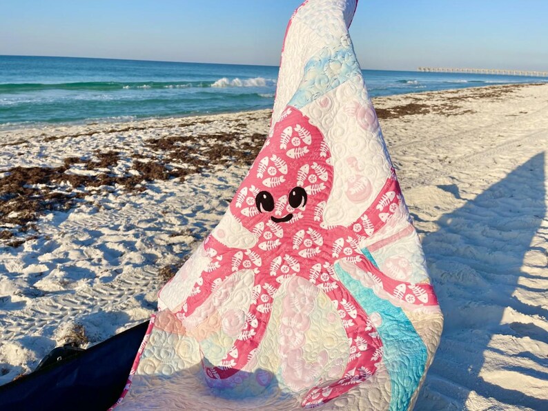 Beach photo of baby octopus applique quilt made with both sides of pink fishbone and sand dollar fabric.