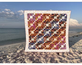 May include: A square quilt featuring a diagonal patchwork pattern of multi-colored floral and abstract fabric squares in shades of pink, orange, blue, and purple, separated by white squares, all framed by a cream-colored border with a leaf pattern.