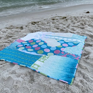 BUBBLES baby whale quilt on the beach with surf.