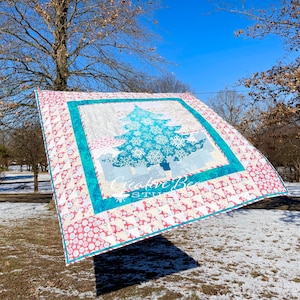 Christmas tree quilt shown blowing from clothesline in snowy scene.