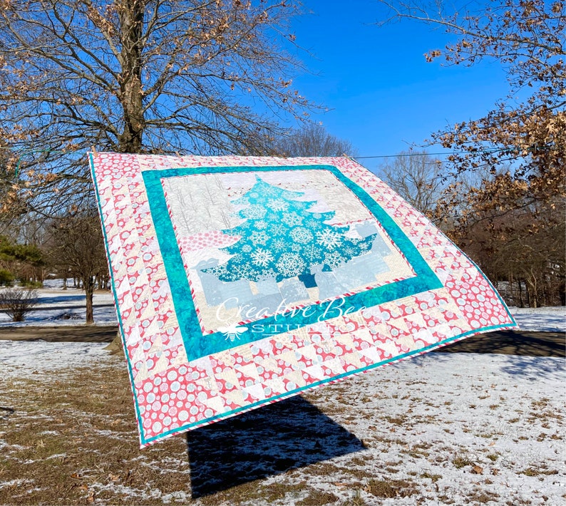 Christmas tree quilt shown blowing from clothesline in snowy scene.
