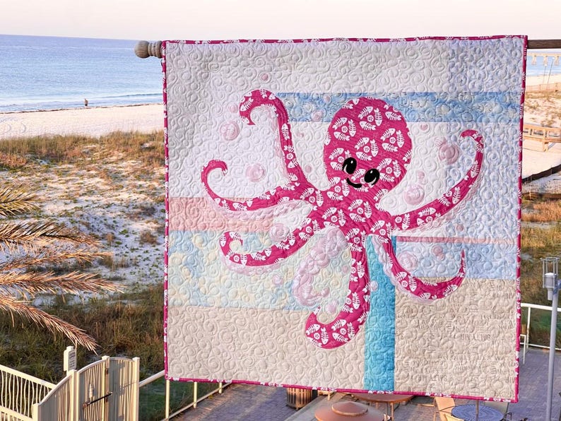Octopus applique quilt hanging at beach scene and made with one focus fabric on a background of eleven scrappy fabrics.