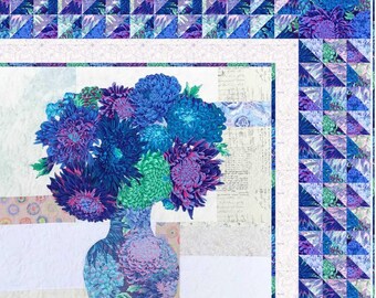 May include: A quilt featuring a central vase filled with blue, purple, and green chrysanthemum flowers. The background consists of white and light-colored fabric blocks with script text. The border is composed of small blue and purple triangles.