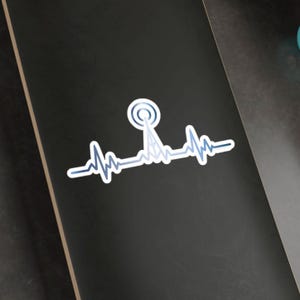 Peut inclure: Un autocollant blanc avec un graphique bleu et blanc d'une antenne radio et d'une ligne de battement de cœur. L'autocollant est sur une surface noire.