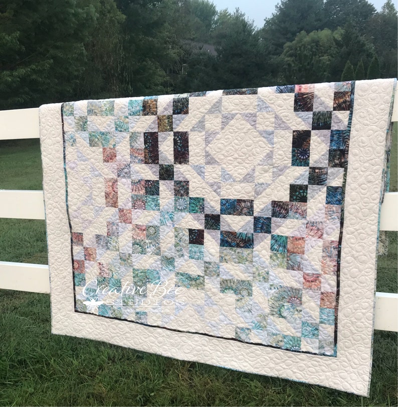 Treasures quilt made with both sides of three fabrics on a white background hanging from white fence.