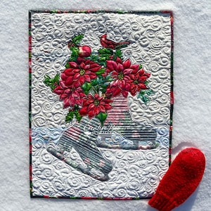 Noelle quilt shown on bed of snow with red mitten.