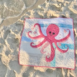Baby octopus quilt shown on sandy beach with sea foam.