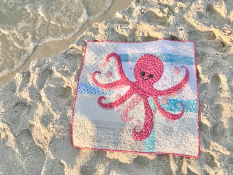Baby octopus quilt shown on sandy beach with sea foam.