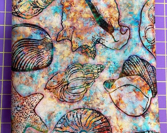 May include: A rectangular piece of fabric featuring a repeating pattern of various seashells and starfish. The design uses a watercolor-style background in shades of blue, orange, and tan, with black outlines defining each shell and sea creature.