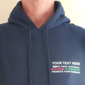 May include: A navy blue hooded sweatshirt with a white pocket and a white embroidered design that says "YOUR TEXT HERE Lots of Fonts And Colors INCLUDING FLUORESCENT PROMOTE YOUR BUSINESS".