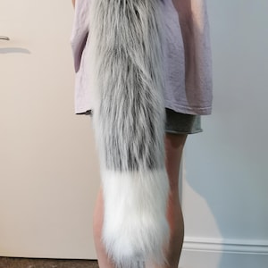 May include: A long, fluffy grey and white tail with a white tip. The tail is made of faux fur and is ideal for cosplay or costume use.