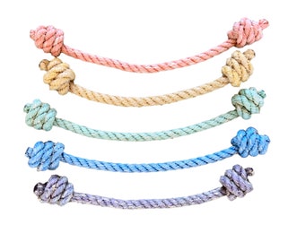 May include: Five colorful rope segments with knotted ends. The ropes are in shades of pink, tan, light green, blue, and purple. Each rope has a knot at both ends, creating a decorative or functional design.