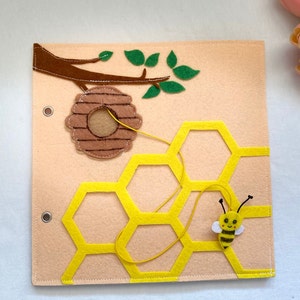 May include: A felt beehive activity board with a yellow honeycomb, a brown felt beehive, and a yellow felt bee with a black and white striped body. A string is attached to the beehive and can be threaded through the honeycomb.