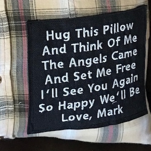 May include: A black pillow with white embroidered text that reads "Hug This Pillow And Think Of Me The Angels Came And Set Me Free I'll See You Again So Happy We'll Be Love, Mark".