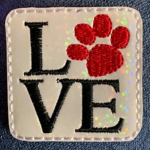 May include: White embroidered patch with the word "LOVE" in black and a red paw print in the center.