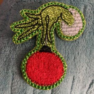 May include: A green and red embroidered Christmas ornament shaped like a cherry with a glittery finish.