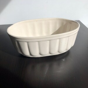 May include: White ceramic oval planter with a ribbed design. The planter is empty and sitting on a dark surface.