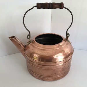 May include: A vintage copper kettle with a wooden handle and a wire bail. The kettle has a hammered finish and is in good condition.