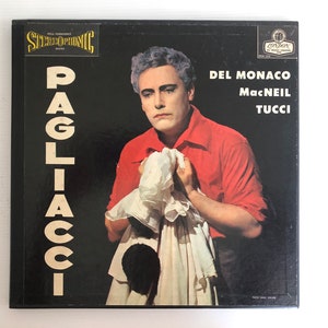 May include: A black and white record album cover featuring a man in a red shirt and white collar, holding a white handkerchief. The album title is "PAGLIACCI" in large white letters. The album features the performers Del Monaco, MacNeil, and Tucci.