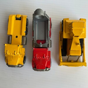 May include: Three toy vehicles: a yellow dump truck, a yellow flatbed truck, and a red dump truck. The trucks are all made of metal and have plastic wheels.