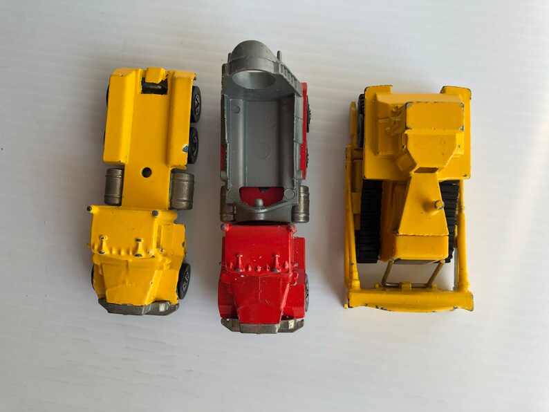 May include: Three toy vehicles: a yellow dump truck, a yellow flatbed truck, and a red dump truck. The trucks are all made of metal and have plastic wheels.